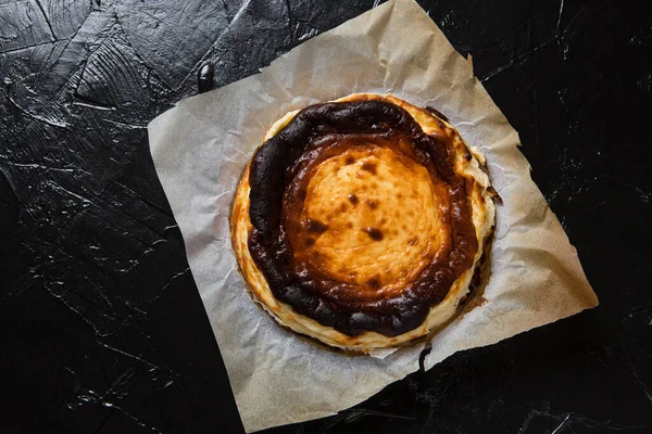 Yeni pişmiş Bask peynirli keki parşömen kağıdında, siyah tahtada, düz yerde.
