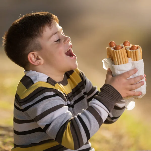4匹のホットドッグを口を開けて食べたいかのように口を開けた陽気な少年の肖像画 コンセプト ストック画像