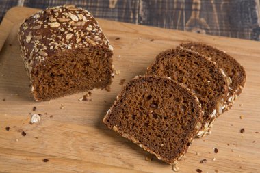 Bir somun çavdar ekmeği ve keten ve ayçiçeği tohumlarıyla dilimlenmiş üç parça. Kesme tahtasında, yakın plan.