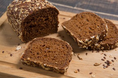 Bir somun kahverengi ekmek, kısmen parçalanmış keten tohumu, ayçiçeği tohumu ve yulaf ezmesi ile kesim tahtasında, yakın plan