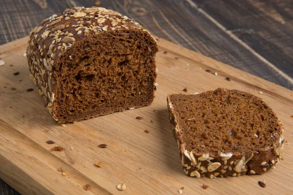 木のまな板の上には 種のあるライ麦パンのパンとそれから切断された部分 健康的な食べ物 クローズアップ — ストック写真