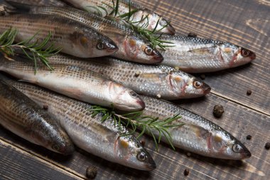 Yığınla gümüş kefal, baharat ve yeşil biberiye filizi, eski tahtalarda, kır tarzı, yakın plan