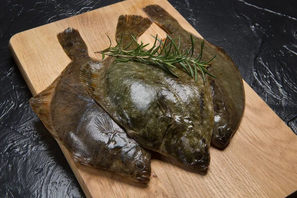 stock image Three fresh raw flounders and sprigs of rosemary on a cutting board, sea fish, diagonal arrangement