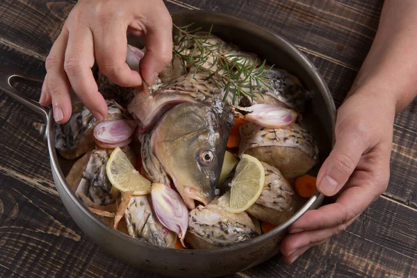 The hands of the cook put the head of a carp in a pan with fish meatballs, an exquisite fish dish