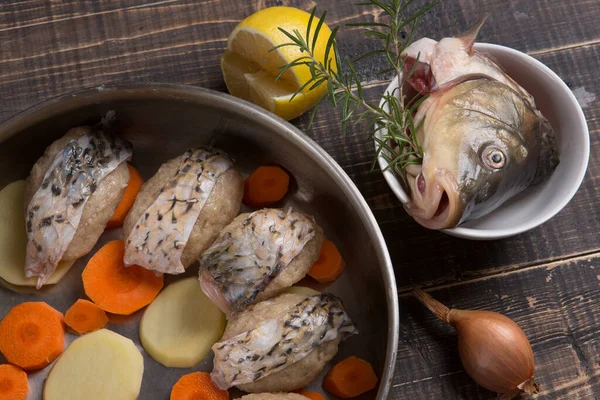 In a frying pan, fish cakes or meatballs decorated with fish skins, next to the frying pan are lemon, onion, fish head and rosemary sprigs