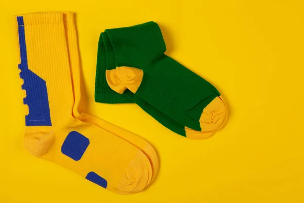 A pair of green socks and a pair of yellow socks, lie side by side on a yellow background, concept