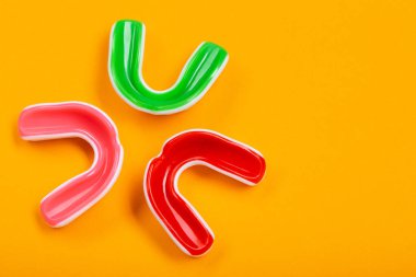 Üç boks ağız koruyucusu, kırmızı, pembe ve yeşil, sarı arka plan, konsept, üst görünüm, kopyalama alanı