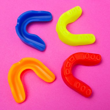 Dört renkli boks ağız koruyucusu pembe arka planda yatıyor.