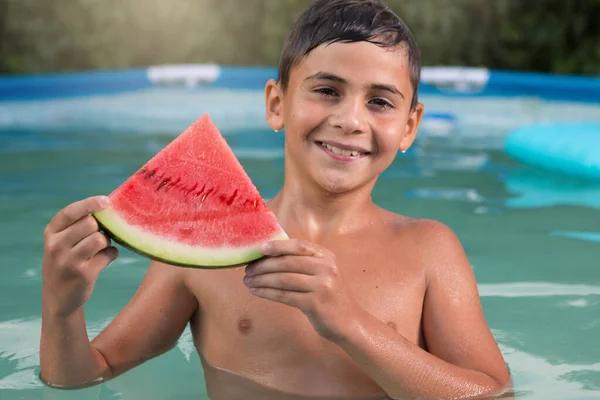 wet boy in the pool with a slice of red watermelon, boy laughing, summer concept