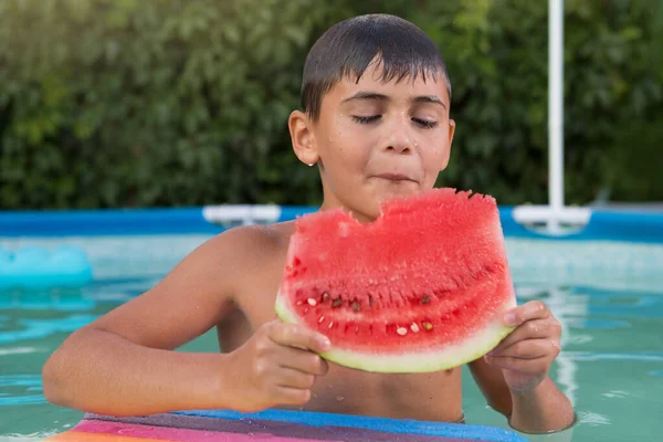 wet boy in the pool eating a big piece of watermelon, summer vacation