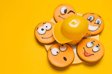 a bunch of smiley cookies on a plate on a yellow background, beside a decorative baseball cap, children's gingerbread with different emotions, the concept