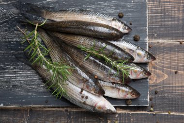 Nine fresh mullets lie on a black board, surrounded by spices and sprigs of rosemary, rustic style, flat lay
