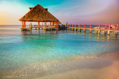 Tropical paradise, sand beach in caribbean with palapa and pier at sunset, Cancun, Mexico