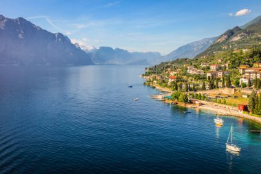 Above idyllic Lake Garda with alps and sailboats in Malcesine at sunrise, Italian alps
