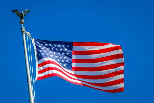 American flag waving on pole with eagle and bright vibrant red white and blue colors against blue sky
