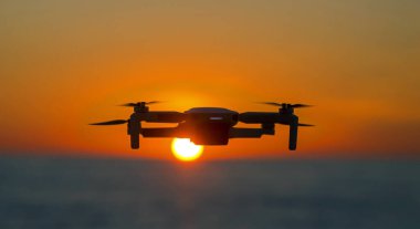 Parlak bir günbatımının arkaplanına karşı gökyüzünde uçan dron. Doğayı gözlemlemek ve filme almak için video kameralı radyo kontrollü bir kuadkopter..