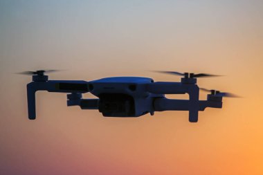 Parlak bir günbatımının arkaplanına karşı gökyüzünde uçan dron. Doğayı gözlemlemek ve filme almak için video kameralı radyo kontrollü bir kuadkopter..