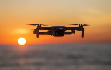 Parlak bir günbatımının arkaplanına karşı gökyüzünde uçan dron. Doğayı gözlemlemek ve filme almak için video kameralı radyo kontrollü bir kuadkopter..