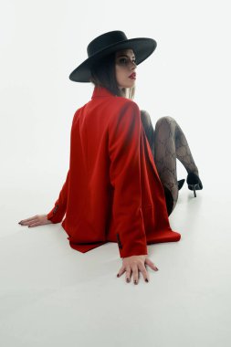 Young girl in a hat and a red jacket poses in the studio