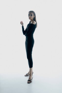 Stüdyoda siyah elbiseyle poz veren zarif genç bir kadının portresi.