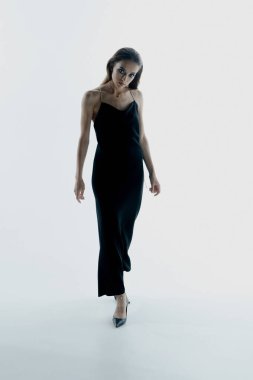 Stüdyoda siyah elbiseyle poz veren zarif genç bir kadının portresi.