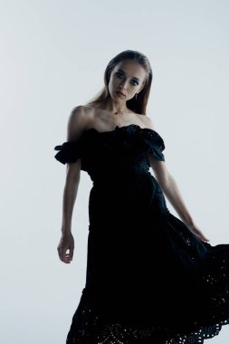 Stüdyoda siyah elbiseyle poz veren zarif genç bir kadının portresi.