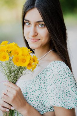 Şapkalı güzel bir kız ve elinde bir buket çiçekle ormanda yürüyor..