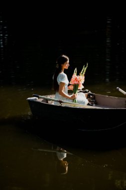 Güzel genç bir kız sabah erkenden elinde bir buket çiçekle bir orman gölünde yelken açıyor.