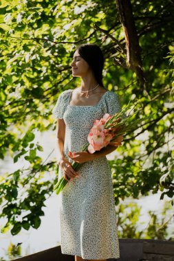 Güzel genç bir kız sabah erkenden elinde bir buket çiçekle bir orman gölünde yelken açıyor.