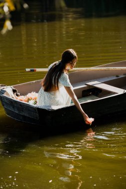 Güzel genç bir kız sabah erkenden elinde bir buket çiçekle bir orman gölünde yelken açıyor.