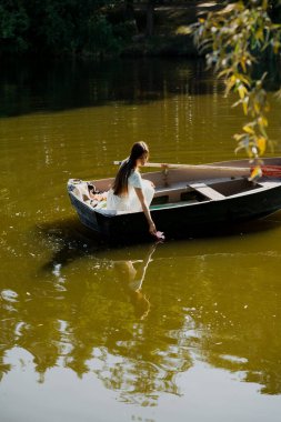 Güzel genç bir kız sabah erkenden elinde bir buket çiçekle bir orman gölünde yelken açıyor.
