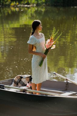 Güzel genç bir kız sabah erkenden elinde bir buket çiçekle bir orman gölünde yelken açıyor.