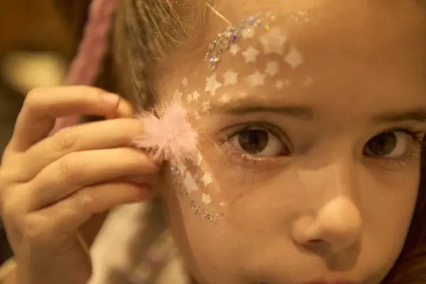 stock image close-up of sweet charming girl looking at the camera in a deep and penetrating way, with white stars and glitter running across her face, while her small hand holds a feather caressing her cheek