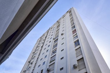 Çok sayıda penceresi ve dikey çizgileri olan büyük beton binanın alt manzarası uzunluğunu artırıyor. Arkaplan olarak açık mavi gökyüzü