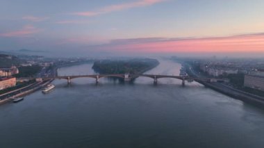 Budapeşte Margaret Köprüsü ya da Margit 'in hava manzarası Tuna Nehri' nin üzerinde gün doğumunda toprak setin üzerinde gizlendi. Şehirde toplu taşıma. Sarı tramvay köprüden geçiyor.