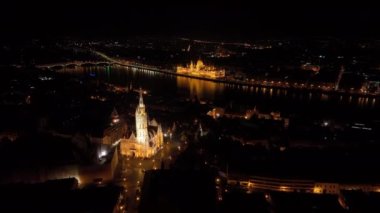 Macaristan 'ın Budapeşte kenti, ünlü Balıkçı Kalesi ve Matthias Kilisesi' nin üzerinden Macaristan Parlamentosu 'nun da desteğiyle Tuna Nehri' ne doğru uçuyor. Gece hava görüntüsü