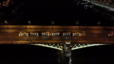 Budapeşte Margaret Köprüsü ya da Margit 'in hava manzarası Tuna Nehri' nin üzerinde, geceleri setin üzerinde saklanıyordu. Şehirde toplu taşıma. Sarı tramvay köprüden geçiyor.