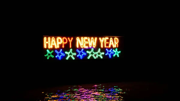 海の水の上に置かれた火の棒で作られた幸せな新年のカラフルな燃焼フレーズ 夜の熱帯の場所での幸せな新年のお祝い ビーチのネオン碑文 — ストック写真