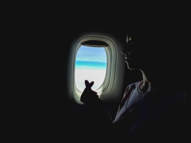 Karanlık tonlarda yaratıcı bir fotoğraf, pencereden dışarı bakan bir kadın, uçakla uçan bir kadın. Kadın, Kore 'nin kalp işareti gibi parmaklarını çapraz yapmış. Seyahat etmeyi severim.