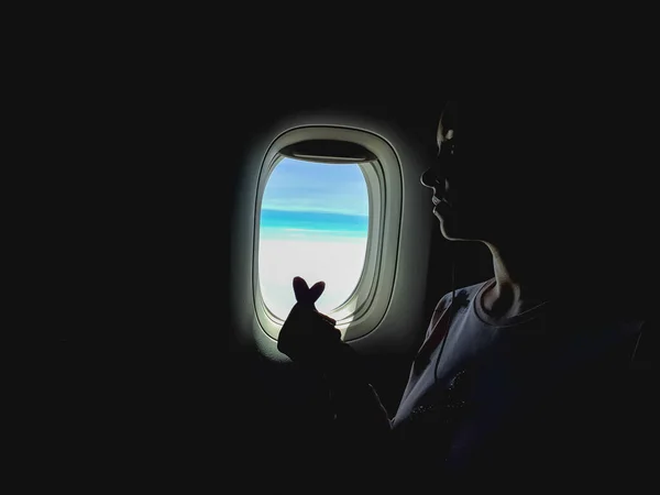 用深沉的色调拍出富有创意的照片 一个女人从飞机窗口往外看 在飞机上飞行 女性像韩国心脏征一样交叉着手指 喜欢旅行 — 图库照片
