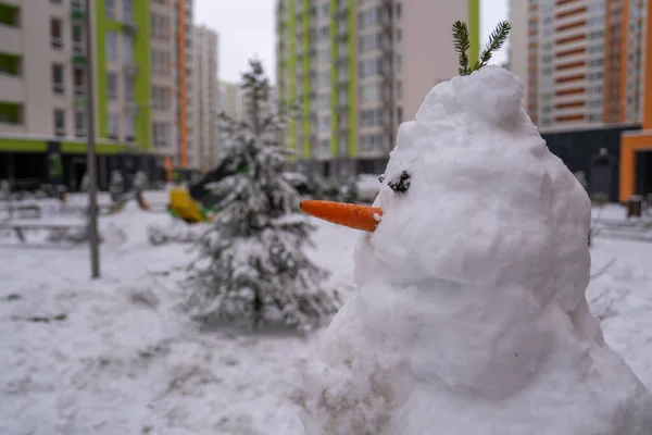 stock image white snowman with carrot nose, made of snow, snowperson built in the backyard of residential apartment in winter. Christmas holidays preparation 