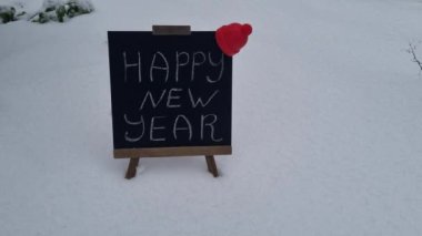 Yeni yılınız kutlu olsun. Tahtaya yazı yazılsın. Taze kar üzerinde duran kardan adam izli kırmızı kupa ve gümüş top. Şenlikli kış tatili