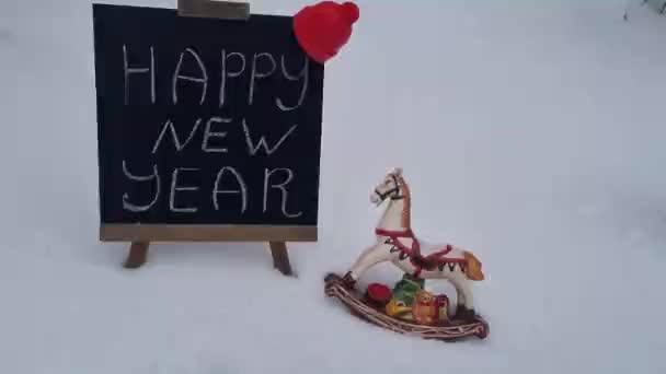 新年快乐 祝你在黑板上写上祝福词 在户外雪地上送上礼物的圣诞装饰玩具马 节日庆祝活动 — 图库视频影像