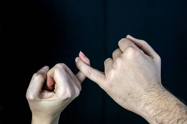 man and woman holding hands on a black background, friendship sign, hold on little fingers, pinky holding hands, make pinky promise, swear gesture, promise has been made, binding