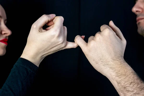 man and woman holding hands on a black background, friendship sign, hold on little fingers, pinky holding hands, make pinky promise, swear gesture, promise has been made, binding