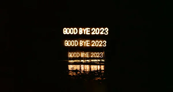 Good bye 2023 triple illuminated sign installation in water on the beach on black. Old year is burning. Happy winter holidays made of lights and garland. Street advertisement. Outdoor signboard.