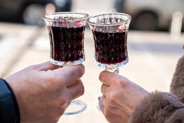 close up of man and woman hands holding two glasses of red wine on the street