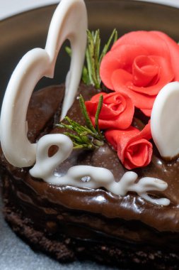 Siyah tabakta romantik çikolatalı pasta. Aziz Sevgililer Günü için sevgi ve kalp mastiği ile süslenmiş küçük bir pasta. Beyaz arka planda izole edilmiş. Romantik tatil randevusu tatlısı