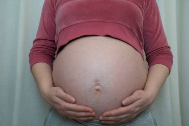 Genç bir kadın hamile karnında ellerini tutuyor. Hamile bir anne. Hamilelik nedeniyle gerilmiş göbek deliği