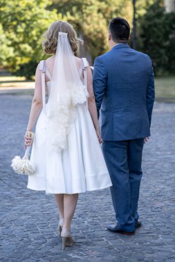 Düğün günü. Gelin ve damat el ele tutuşuyor. Yeni evli çiftimiz fotoşopesyon için dışarıda poz veriyor. Tüm vücut 